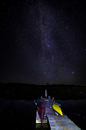 Boat dock under a starry sky as meteor streaks across the Milky